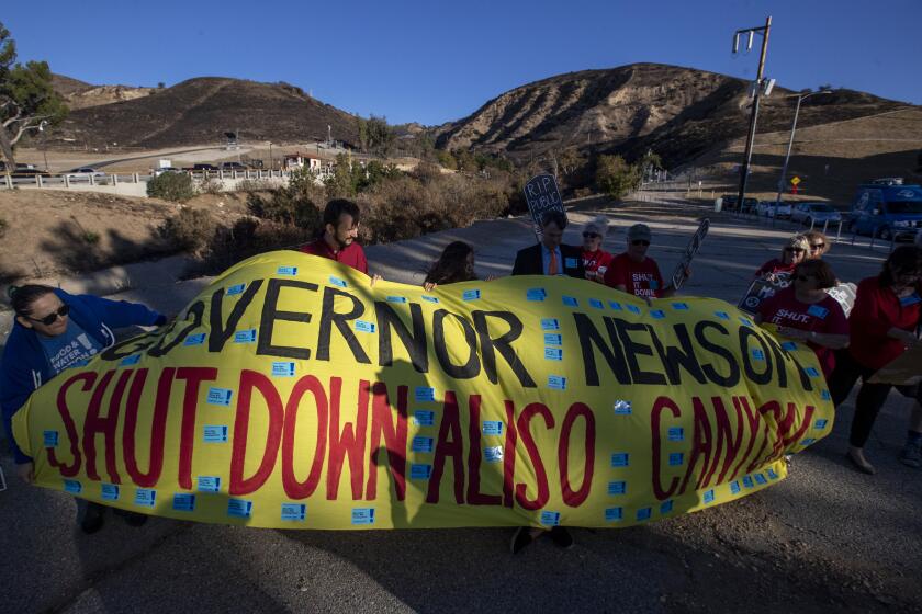 PORTER RANCH, CALIF. -- WEDNESDAY, OCTOBER 23, 2019: North San Fernando Valley residents struggle to unfurl a banner in windy conditions during a rally marking the fourth anniversary of the SoCal Gas company’s Aliso Canyon gas facility blowout in Porter Ranch, Calif., on Oct. 23, 2019. (Brian van der Brug / Los Angeles Times)