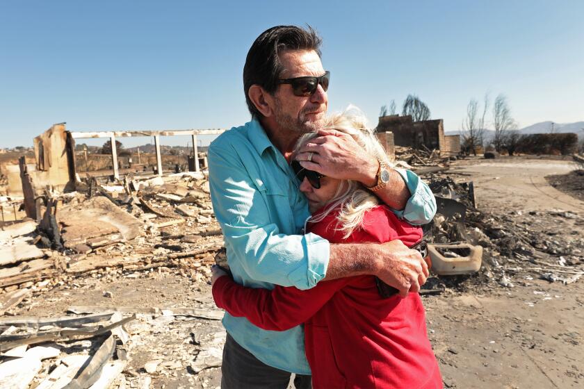 Camarillo, CA - November 08: Las Posas Hills on Friday, Nov. 8, 2024 in Camarillo, CA. Homeowners Dr. Stanley Jensen hugs his wife Dawn DaMart as they returned from a trip to Minnesota to their home on the corner of Esteban Drive and Corriente Ct. in the Las Posas Hills neighborhood of Camarillo that was ravaged by the Mountain Fire as homeowners begin to arrive Friday morning to view the aftermath and see what condition their home is in after the Mountain fire tore through Camarillo. The firefighters are assisting her family in the search for a wall safe that holds family heirloom jewelry. (Al Seib / For the Los Angeles Times)