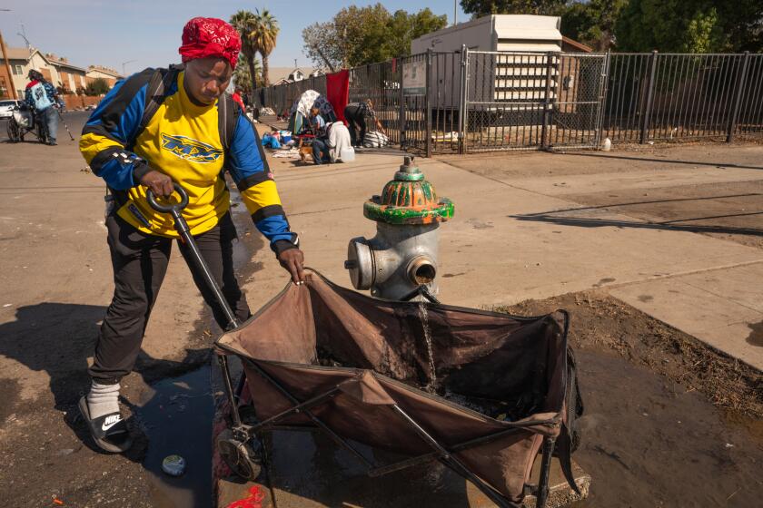 FRESNO, CALIF OCTOBER 30, 2024 - An unhoused woman gets water from a hydrant before Fresno city's pending demolition of homeless encampment on Santa Clara Street in Fresno. (Tomas Ovalle / For The Times)