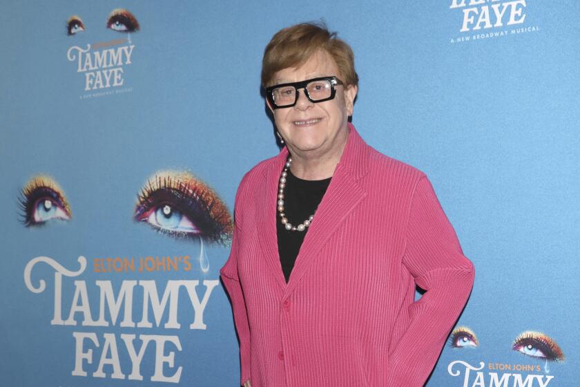 Elton John poses in pink corduroy suit and black glasses at the Nov. 14 Broadway opening of "Tammy Faye" in New York