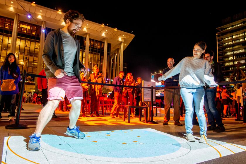 Two young adults place a dance game that is projected on the concrete. 