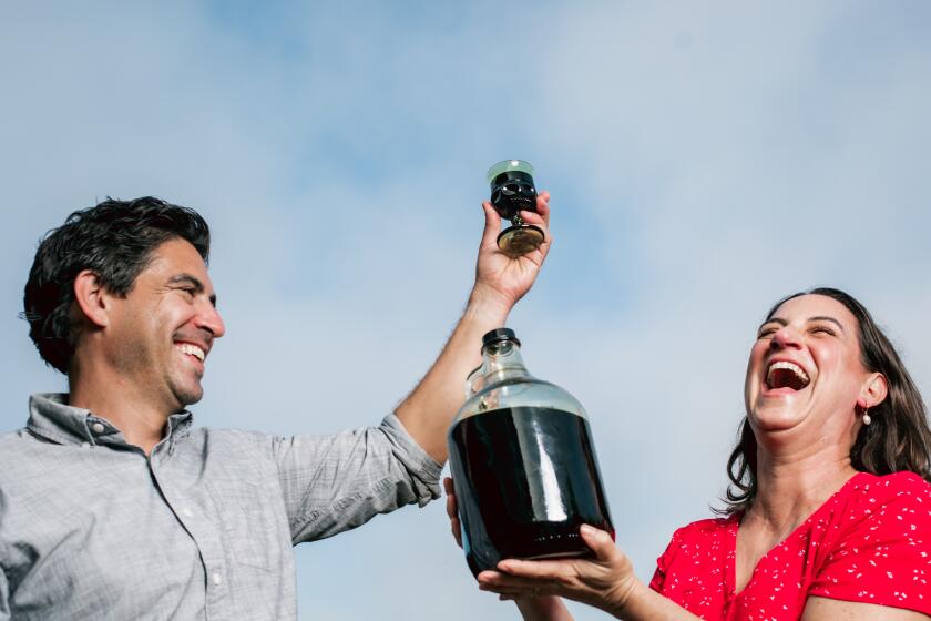 HUNTINGTON BEACH -- OCTOBER 5, 2024: (L-R) Michael Purtill and Corrine Purtill pose with their new batch of nocino created from their great-grandfather's recipe in Huntington Beach on Saturday, October 5, 2024 (Emil Ravelo / For The Times)