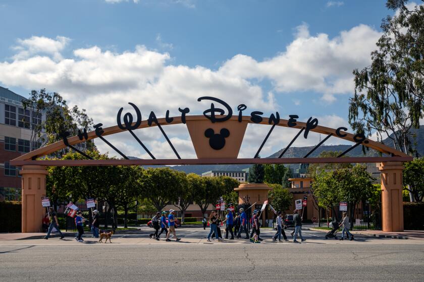 A group of people walking with picket signs underneath the entrance to the Disney studio lot in Burbank