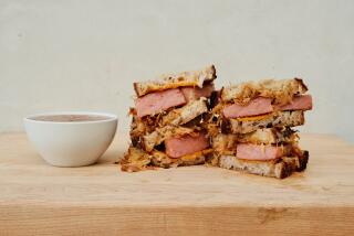 Two stacks of halved fried-spam kimchi grilled cheese sandwiches on a wood board. At side, a bowl of red-brown dipping sauce.