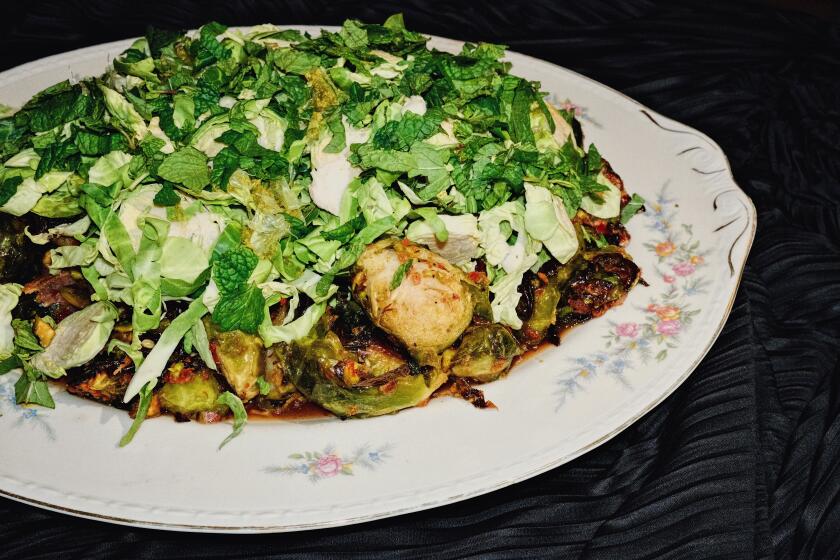 A floral porcelain platter of Brussels sprouts cooked and raw, with bacon, mint and pistachio on a black cloth background