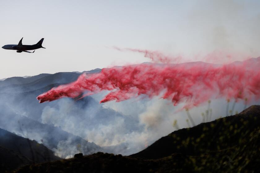 An aircraft drops fire retardant on the Lisa fire burning in a canyon east of Moreno Valley.