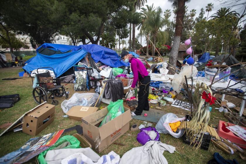 LOS ANGELES, CA - MARCH 25: Valerie Zeller trying to organize her belongings as she is packing outside her tent next other tents at Echo Park Lake Thursday, March 25, 2021 in los Angeles, CA. A fence was put overnight around Echo Park lake last night and the clean up has begun Thursday. People who have been living in tents around the lake were asked to leave and some were helped my agencies to find shelter. (Francine Orr / Los Angeles Times)