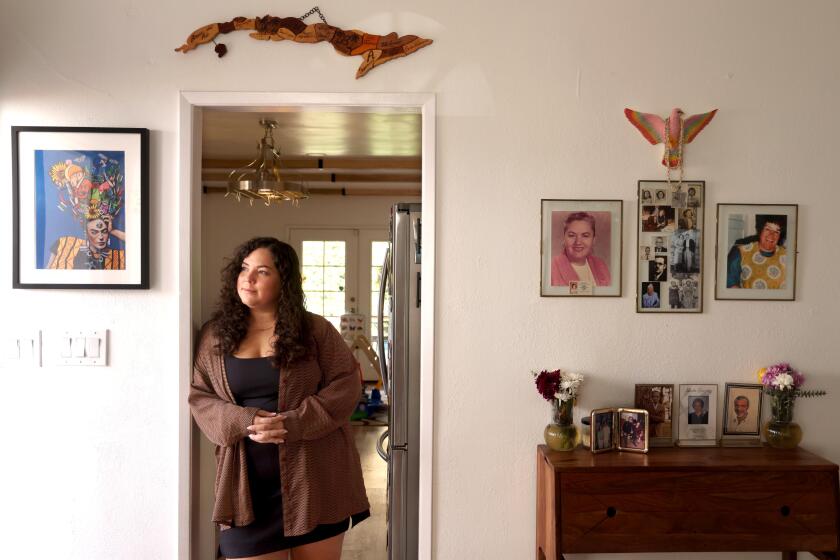 Diandra Kendall Luzon leans against a doorframe in a white wall decorated with framed art and family portraits.