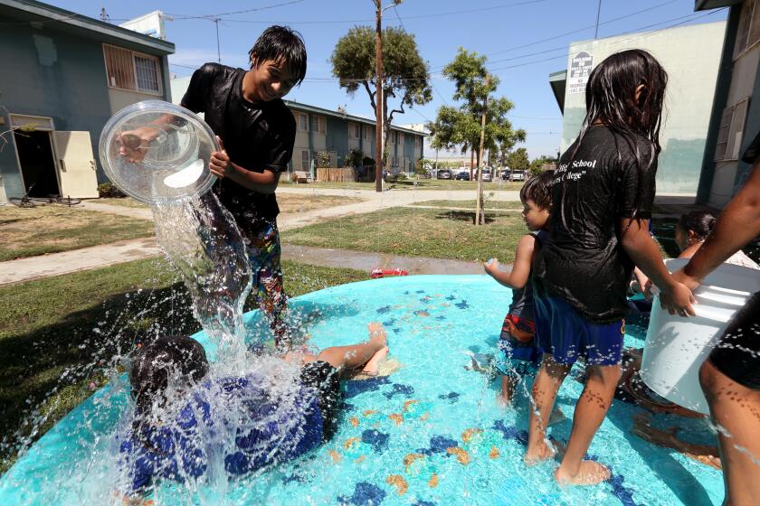 WATTS, CA - AUGUST 1, 2023 - Miguel Mendoza, 13, pours water on one of his relatives while cooling off in an inflatable pool outside his home at the Imperial Courts housing project in Watts on August 1, 2023. Watts has been the site of violence in recent weeks with multiple people dying and 9 people being shot in Imperial Courts and Jordan Downs housing projects. (Genaro Molina / Los Angeles Times)